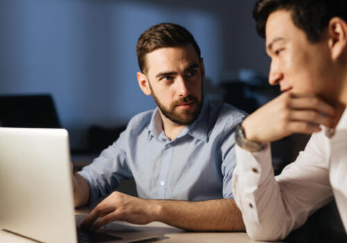 Small group of young businessmen discussing sales statistics late in the evening in office